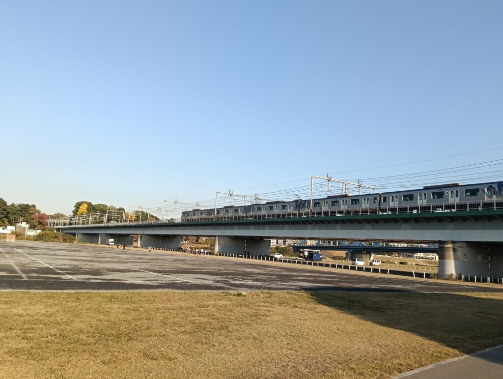 電車が橋の上を走っている。一級河川（多摩川）の広大な河川敷が見える。