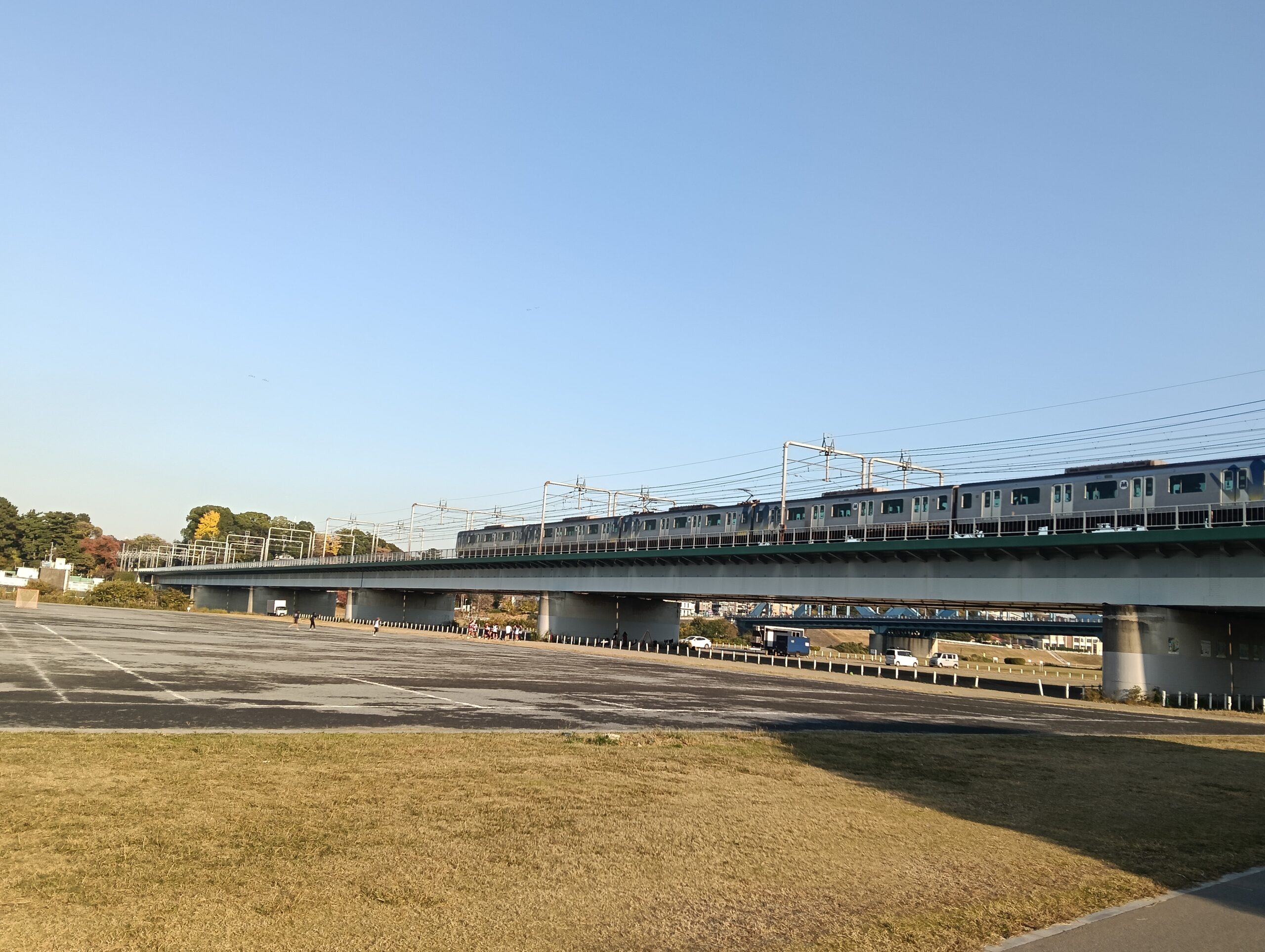 電車が橋の上を走っている。一級河川(多摩川)の広大な河川敷が見える。